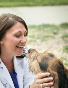A veterinarian in a white coat smiling at a beagle she is holding